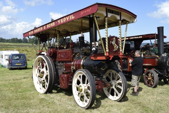 Vintage steam-driven tractor with wooden canopy and large spoked wheels in a grassy field.