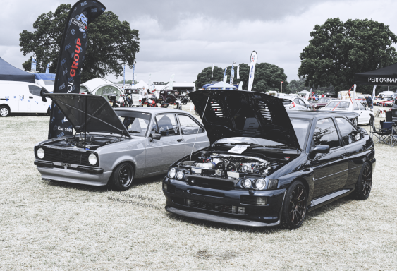 Two modified cars parked side by side with bonnets open, showcasing their engines.