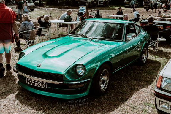 A green vintage sports car parked at an outdoor event with people in the background.