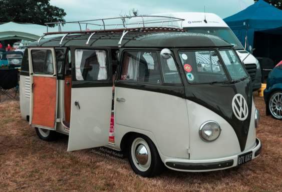 Vintage Volkswagen van with two open side doors, parked on grass.