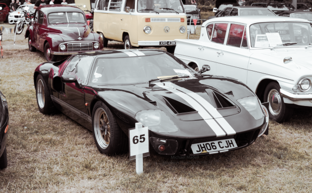 Black sports car with white stripes parked among classic vehicles.