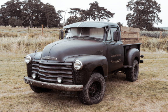 Vintage black pickup truck parked on grass with trees in the background.