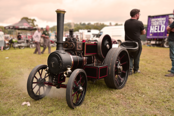 Vintage steam engine with small wheels and a black chimney, parked on grassy terrain.